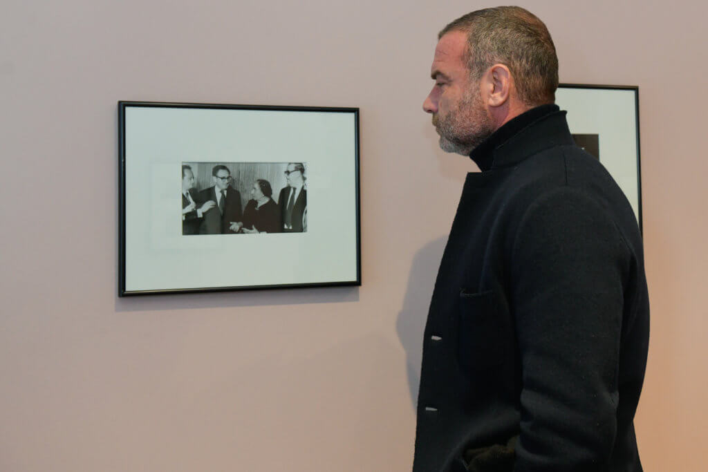 Liev Schreiber looking at picture of Henry Kissinger